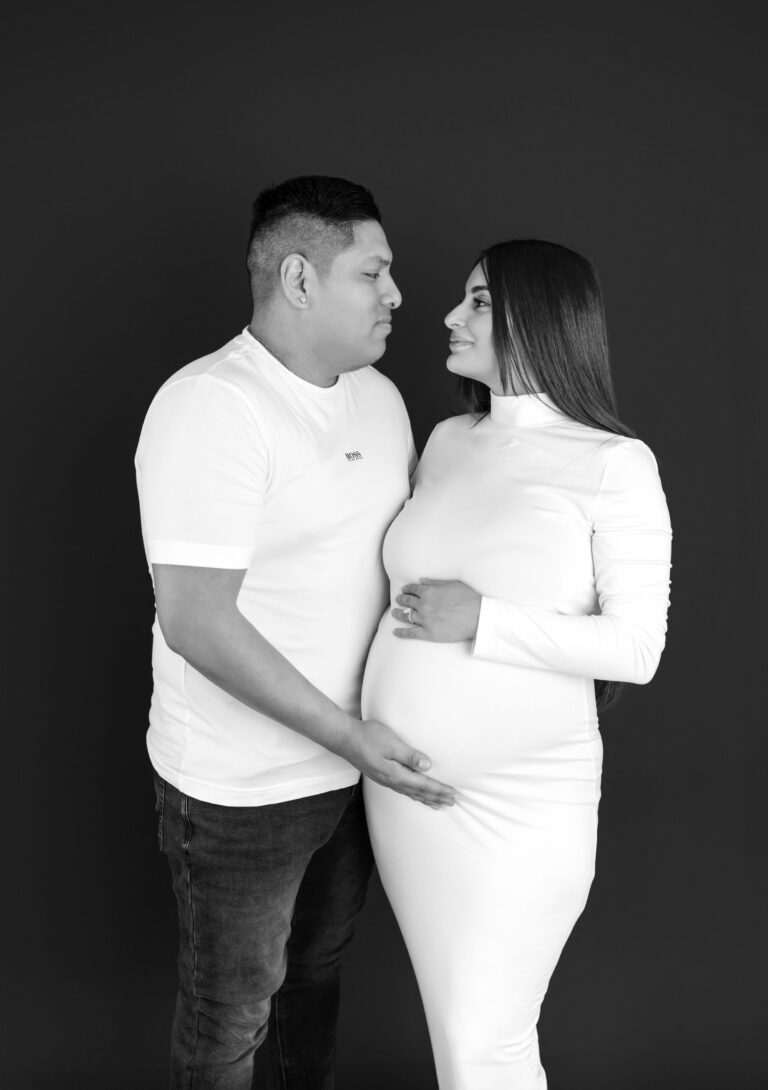 Couple Holding Baby Bump And Looking At Each Other During A Maternity Photo Shoot In Black And White